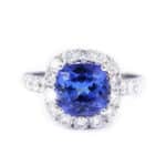 Engagement ring with a cushion-cut blue sapphire center surrounded by a halo of diamonds on a diamond-studded band.