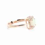Rose gold ring with a pale gemstone surrounded by a diamond halo on a white background, close-up detail.