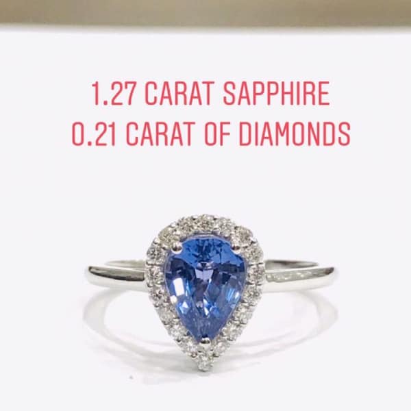 Ring with a pear-cut blue sapphire surrounded by a diamond halo on a silver band; labeled 1.27 ct sapphire and 0.21 ct diamonds.