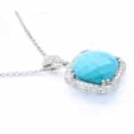 Silver necklace with a turquoise-blue cushion-cut gemstone encircled by small diamonds on a delicate chain, close-up view